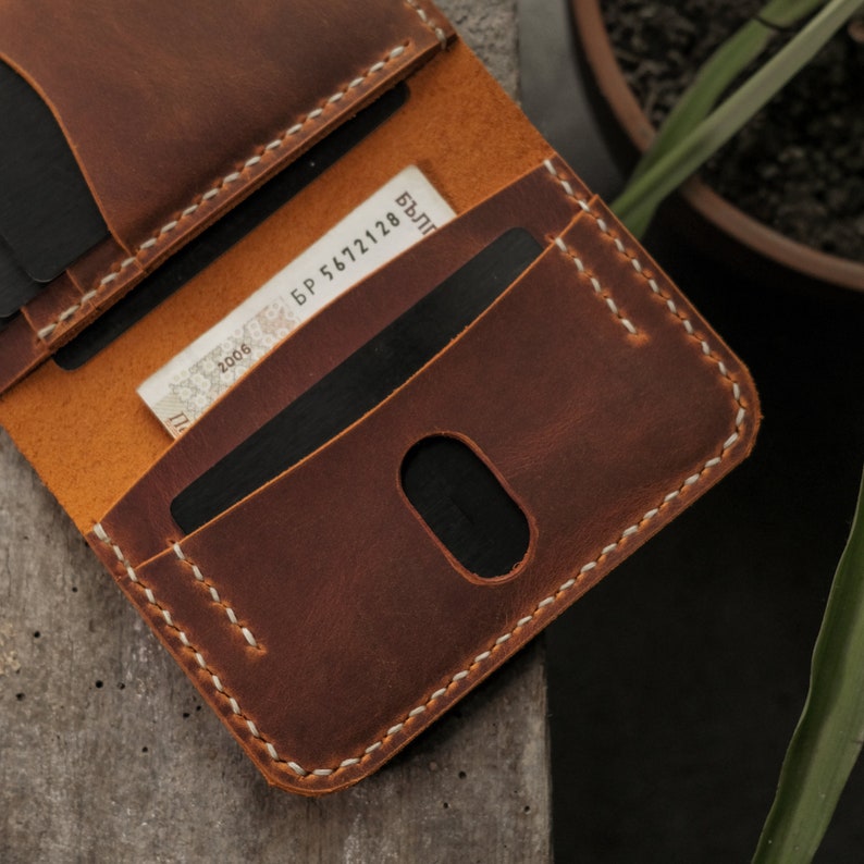 Card slot detail showing oval-shaped thumb notch cutout in camel crazy horse leather, designed for easy card removal. Folded cash compartment visible in center. Natural grain texture and matte waxy finish characteristic of crazy horse leather treatment.