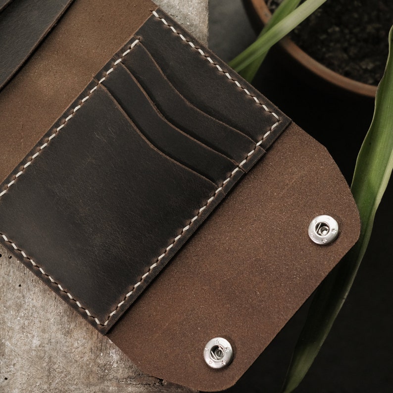 Taupe crazy horse leather wallet exterior showing natural color variation between outer surface and lighter edge finishing. Two brass snap closures provide secure closure. Leather displays characteristic matte waxy finish with subtle grain pattern.