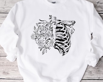 May include: White sweatshirt with a black and white graphic print of a ribcage and flowers. The graphic is centered on the front of the sweatshirt.