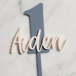 May include: A white ceramic mug with a black handle and the text "But First, Coffee" in a bold, black font. The mug is set against a blurred background, highlighting its clean design.