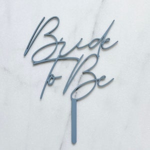 Könnte beinhalten: Ein hellblauer Tortendekor mit den Worten "Bride to Be" in kursiver Schrift.