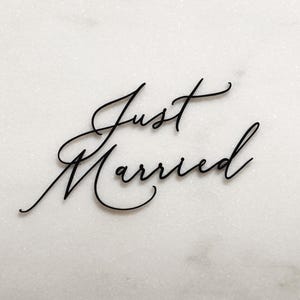 Op de afbeelding: Zwarte kalligrafie op een witte achtergrond met de tekst "Just Married".