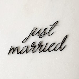 Könnte beinhalten: Schwarzer Schreibschrift-Text auf weißem Hintergrund: "just married". Die elegante Schrift ist eine beliebte Wahl für Hochzeitsdekorationen, Tortenaufsätze oder Foto-Requisiten. Die Buchstaben sind verbunden und erzeugen ein fließendes, romantisches Gefühl.