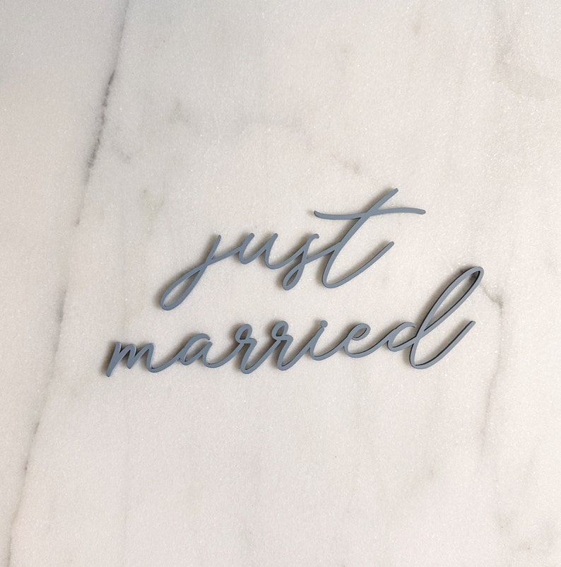 Puede incluir: Un letrero de madera gris con las palabras "just married" en una fuente cursiva.