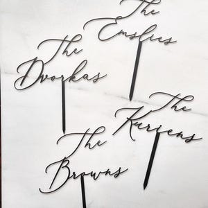 K&ouml;nnte beinhalten: Schwarze, lasergeschnittene Tortenaufs&auml;tze mit den Namen "The Dvoraks", "The Emslies", "The Browns" und "The Kurzens" in eleganter Schrift. Jeder Aufsatz hat einen Stab zum einfachen Einstecken in einen Kuchen. Ideal f&uuml;r Hochzeiten oder Familienfeiern.
