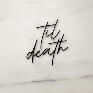 May include: Black calligraphy script on a white marble background that reads "til death".
