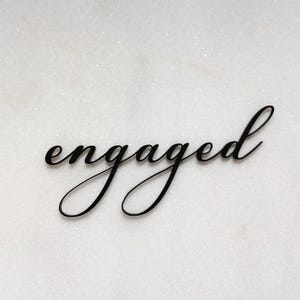 May include: Black cursive script lettering that reads "engaged" on a white background.