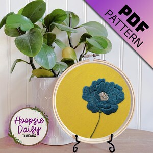 May include: A PDF pattern for a blue flower embroidery design on a yellow background. The pattern is displayed in a wooden embroidery hoop.