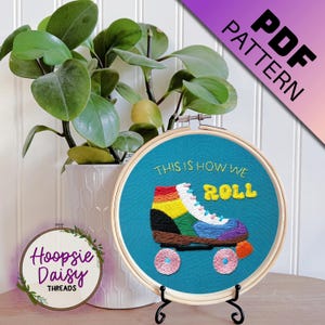 May include: Embroidered hoop art with a teal background featuring a rainbow roller skate with the text "This is how we roll" in yellow.