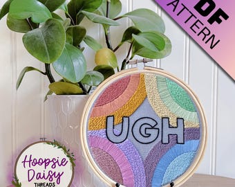 May include: Embroidered hoop art with the word "UGH" in black letters on a gray background. The background is filled with colorful rainbow-like arcs of embroidery floss.