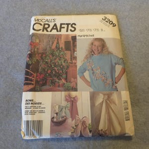May include: A McCall's Crafts sewing pattern envelope, number 3209, featuring a light blue long-sleeve sweater decorated with fabric bows. The cover displays images of a decorated Christmas tree and various bow designs for home decor.