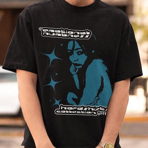 May include: Black t-shirt with the text "emotional numbness" above a teal illustration of a person. The shirt also has the text "hardshirt collection" below the illustration. The shirt is short-sleeved.