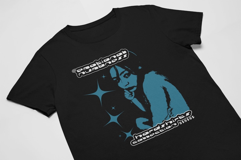 May include: Black t-shirt featuring a teal graphic of a person with a finger to their lips, surrounded by star shapes. The shirt has the text "emotional numbness" and "hardshirts collection" in a retro font.