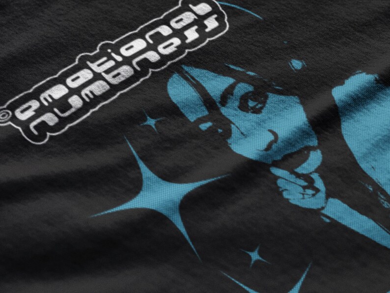 May include: Black t-shirt featuring a stylized illustration of a person with blue accents and starburst shapes. The text "emotional numbness" is printed in white, in a rounded, stylized font.