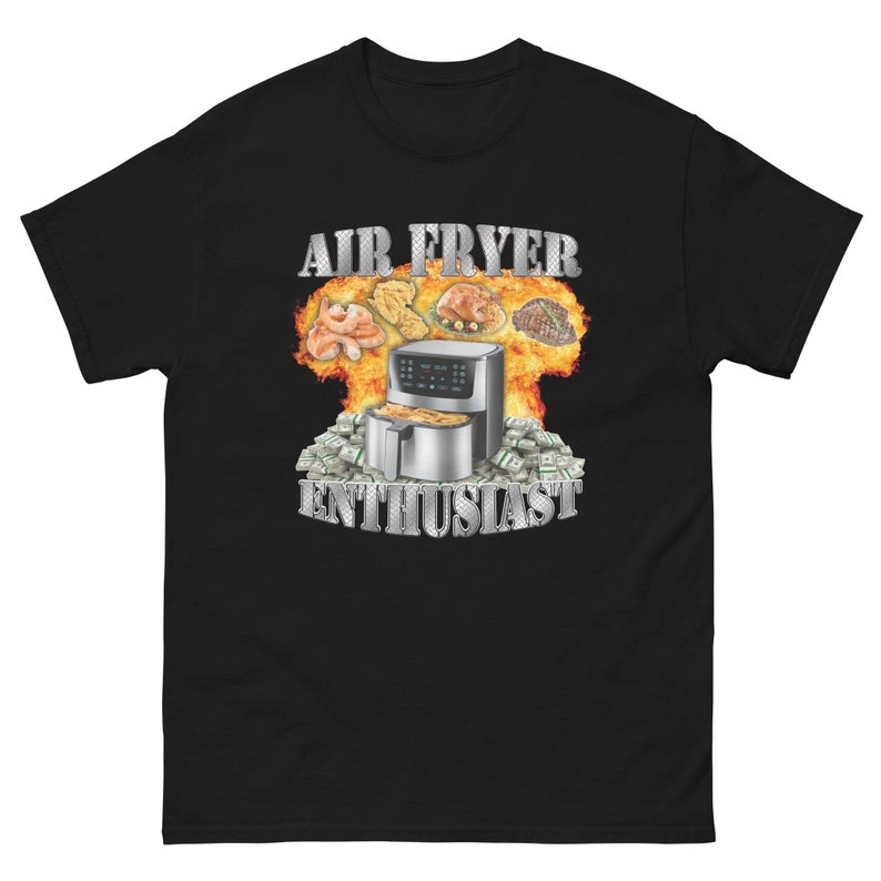 Pode incluir: Camiseta preta com as palavras "AIR FRYER ENTHUSIAST" em letras prateadas. O gr&aacute;fico apresenta uma fritadeira a ar rodeada por chamas e v&aacute;rios alimentos cozidos, com pilhas de dinheiro na base.
