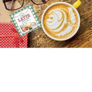 May include: A green and white gift tag with the text "Thanks a Latte for all you do! We appreciate you!" and a drawing of a latte with whipped cream and sprinkles. The tag is sitting on a wooden surface next to a red gift box with white stars and a cup of latte with latte art.