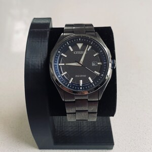May include: A black Citizen Eco-Drive watch with a silver stainless steel band. The watch face is black with silver hands and markers. The watch is on a black watch stand.