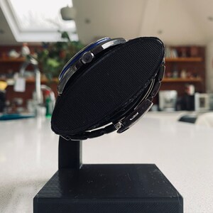 May include: A silver watch with a blue face and a black watch stand. The watch is on the stand and the face is facing the camera.