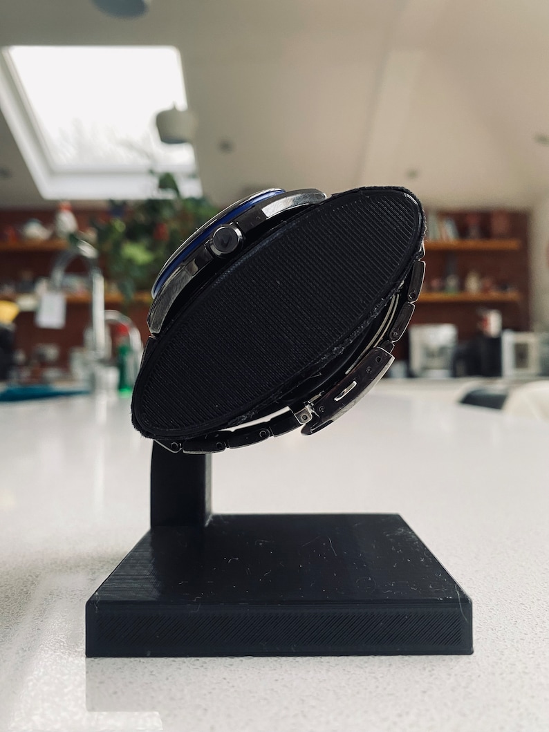 May include: A silver watch with a blue face and a black watch stand. The watch is on the stand and the face is facing the camera.