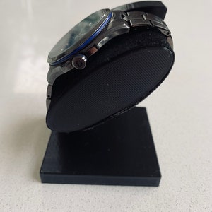 May include: A silver watch with a black face and a blue ring around the edge of the face. The watch is on a black watch stand.