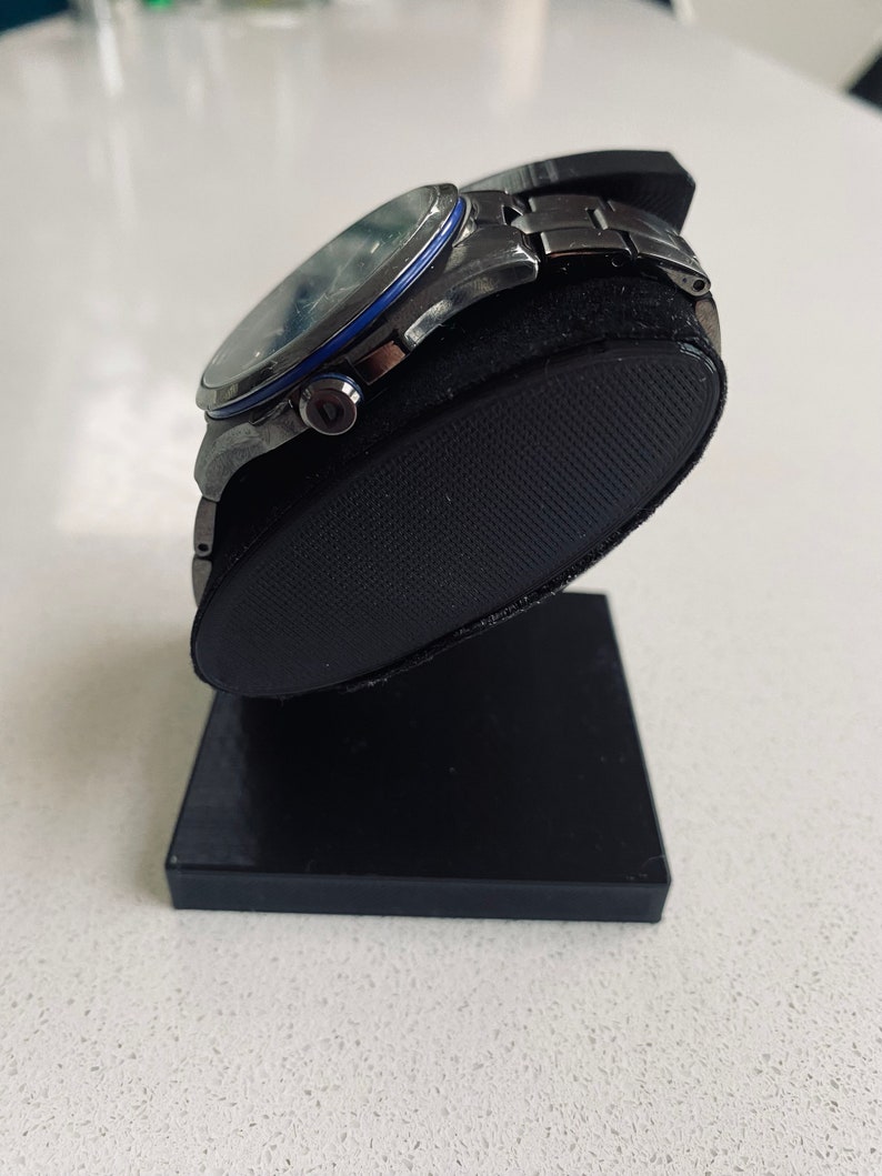 May include: A silver watch with a black face and a blue ring around the edge of the face. The watch is on a black watch stand.