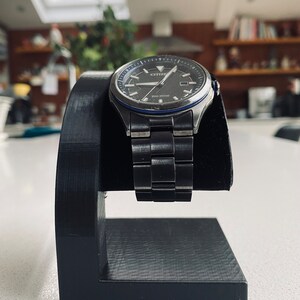 May include: A black watch stand with a silver watch with a black face and blue accents. The watch has the word "CITIZEN" on the face and the words "Eco-Drive" below it.