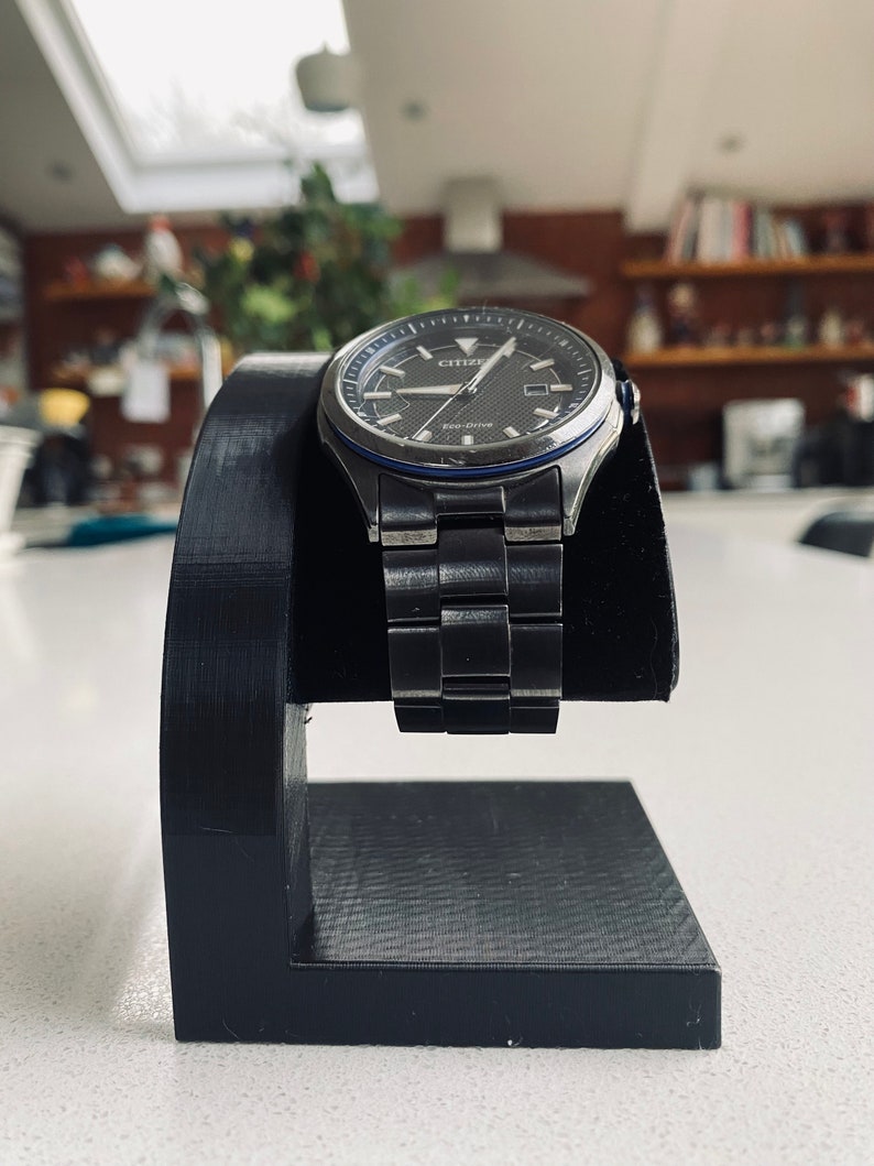 May include: A black watch stand with a silver watch with a black face and blue accents. The watch has the word "CITIZEN" on the face and the words "Eco-Drive" below it.