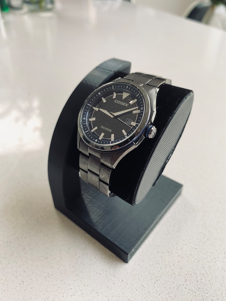 May include: A silver Citizen Eco-Drive watch with a black face and a black leather watch stand.