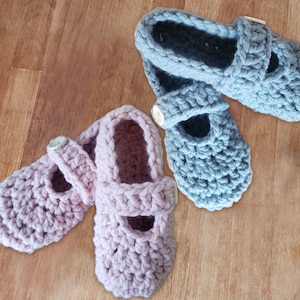 Może przedstawiać: Dwie pary szydełkowych bucików dla niemowląt, jedna para jest różowa, a druga niebieska. Obie pary mają ozdobny guzik.