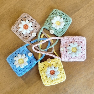 May include: Five crocheted daisy flower purses in different colors, including blue, pink, yellow, green, and brown. Each purse has a small button in the center of the flower.