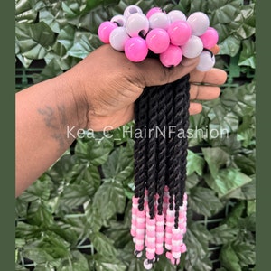May include: A set of black braided hair extensions with pink and white beads at the ends. The beads are in an alternating pattern.