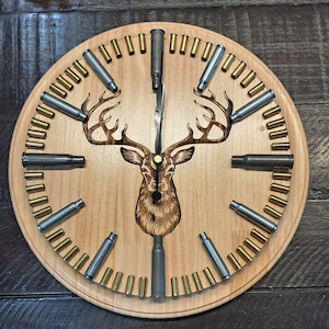May include: A wooden clock with a deer head design and bullet casings around the edge. The clock hands are made of metal.