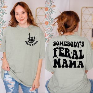 a woman wearing a t - shirt that says somebody's feral mama