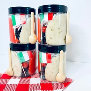 May include: Four clear plastic jars with black lids, each containing play dough, wooden spoons, and decorative elements. The jars are decorated with Italian flags and sit on a red and white checkered cloth.