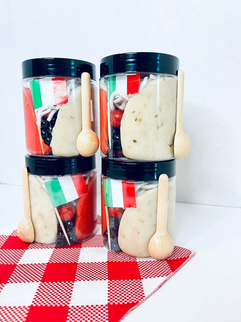 May include: Four clear plastic jars with black lids, each containing play dough, wooden spoons, and decorative elements. The jars are decorated with Italian flags and sit on a red and white checkered cloth.