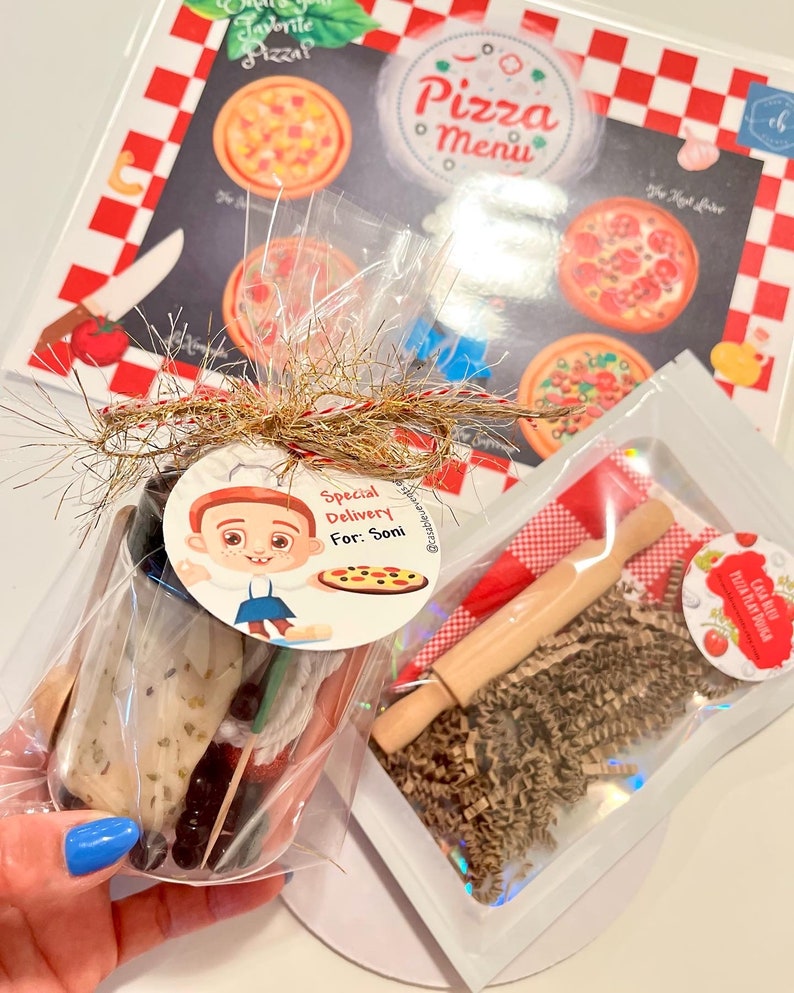 May include: A pizza-themed play set with a pizza menu, a small rolling pin, and play dough. The set includes a pizza menu with various pizza illustrations and a tag that says "Special Delivery For: Soni."