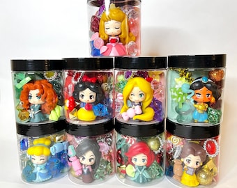 May include: Nine clear plastic jars with black lids, each containing a small cartoon-style princess figurine surrounded by colorful plastic gems, beads, and candy-shaped charms. The collection features various characters with distinct hair colors and outfits.