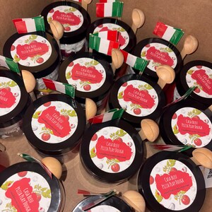 May include: A selection of black-lidded jars, each bearing a label reading "Casa Bleu Pizza Play Dough", accompanied by a small wooden spoon and a miniature Italian flag. The jars are presented in a cardboard box.