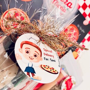 May include: A cellophane-wrapped gift basket with a pizza theme. The basket includes a pizza menu, a tag with a cartoon chef, and the text "Special Delivery For: Soni". The basket is decorated with gold and red tinsel.