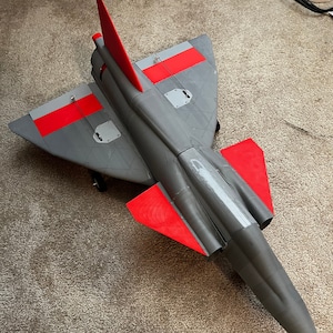 May include: A gray and red model airplane with a long, pointed nose and a single tail fin. The airplane has red accents on the wings and tail.