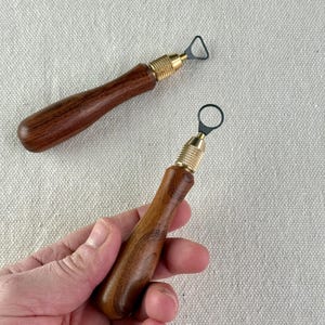 May include: Two pottery tools with wooden handles and brass fittings. One has a triangular cutting head, the other a circular one. These tools are for shaping and carving clay, ideal for ceramic work.