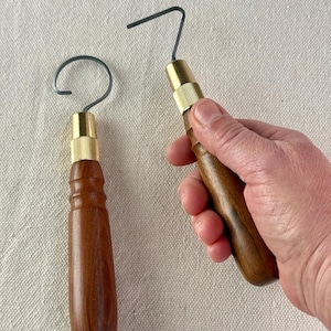 May include: Two tools with wooden handles, brass fittings, and curved metal ends. One is held in a hand. The other rests on a neutral surface. These tools are likely for crafts or woodworking.