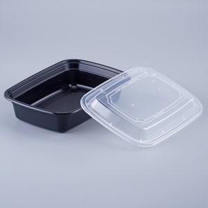Könnte beinhalten: Ein schwarzer Plastikbehälter für Lebensmittel mit einem durchsichtigen Plastikdeckel. Der Behälter ist quadratisch und hat eine glatte Oberfläche. Der Deckel hat einen leicht erhöhten Rand um den Umfang.