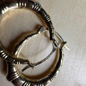 May include: Gold-toned hoop earrings with a bamboo-like design. The earrings have a textured surface and a hinged closure. The metal is stamped with "AU 10K". These earrings are a stylish accessory.