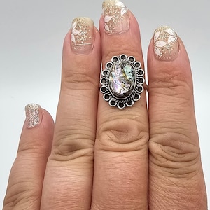 May include: A silver ring with an oval abalone shell set in a decorative silver bezel. The ring is on a finger with a light brown skin tone.