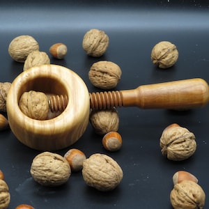 Może przedstawiać: Drewniany łamacz orzechów z korbą i miską na orzechy. Łamacz orzechów jest otoczony orzechami włoskimi i laskowymi.