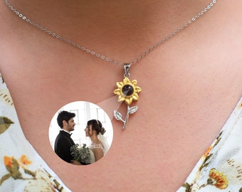 May include: A silver chain necklace with a sunflower pendant. The sunflower has a black centre that reveals a hidden photo when viewed through a magnifying glass. The photo shows a couple in a wedding setting.