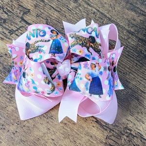 May include: Pink hair bow with a white polka dot pattern and a colorful print of a cartoon character. The print features a girl in a blue dress and a jaguar.