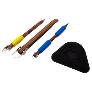 Könnte beinhalten: Ein Set aus drei Holzwerkzeugen mit Metallklingen und farbigen Griffen, darunter Gelb und Blau. Ebenfalls enthalten ist ein schwarzes, dreieckiges Etui mit einem Diamantlogo. Die Werkzeuge scheinen für Bastelarbeiten oder Kunst zu sein.