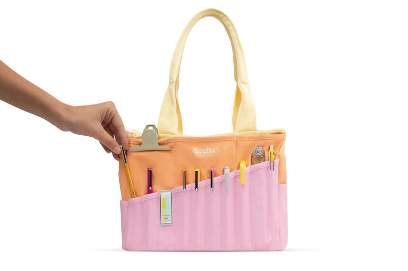 A hand is holding a pencil case with various writing utensils inside, including pens and pencils.